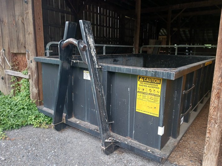 Small black dumpster inside a barn with caution stickers and steel hooks