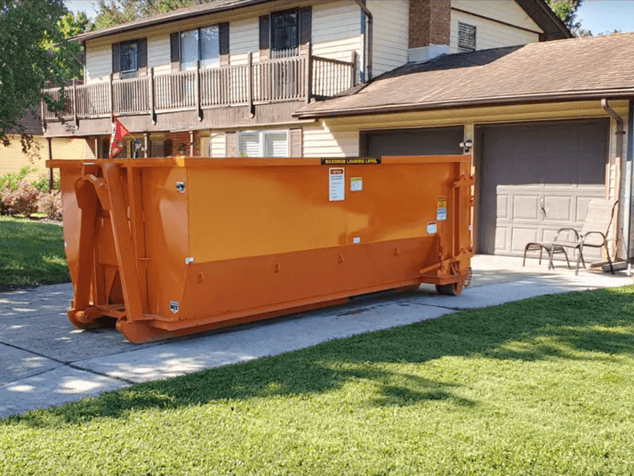 Bright orange residential dumpster rental placed neatly in a driveway surrounded by grass and trees