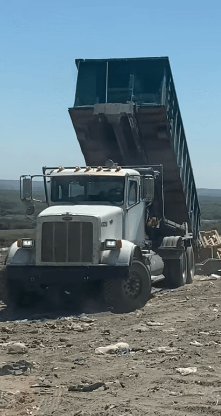 Green roll-off dumpster being unloaded at a landfill from a large truck
