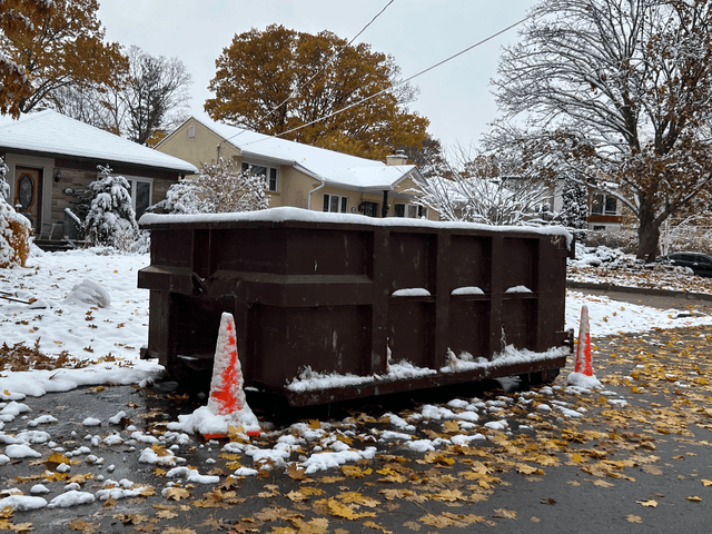 Small roll-off dumpster placed on a residential street with snow and traffic cones